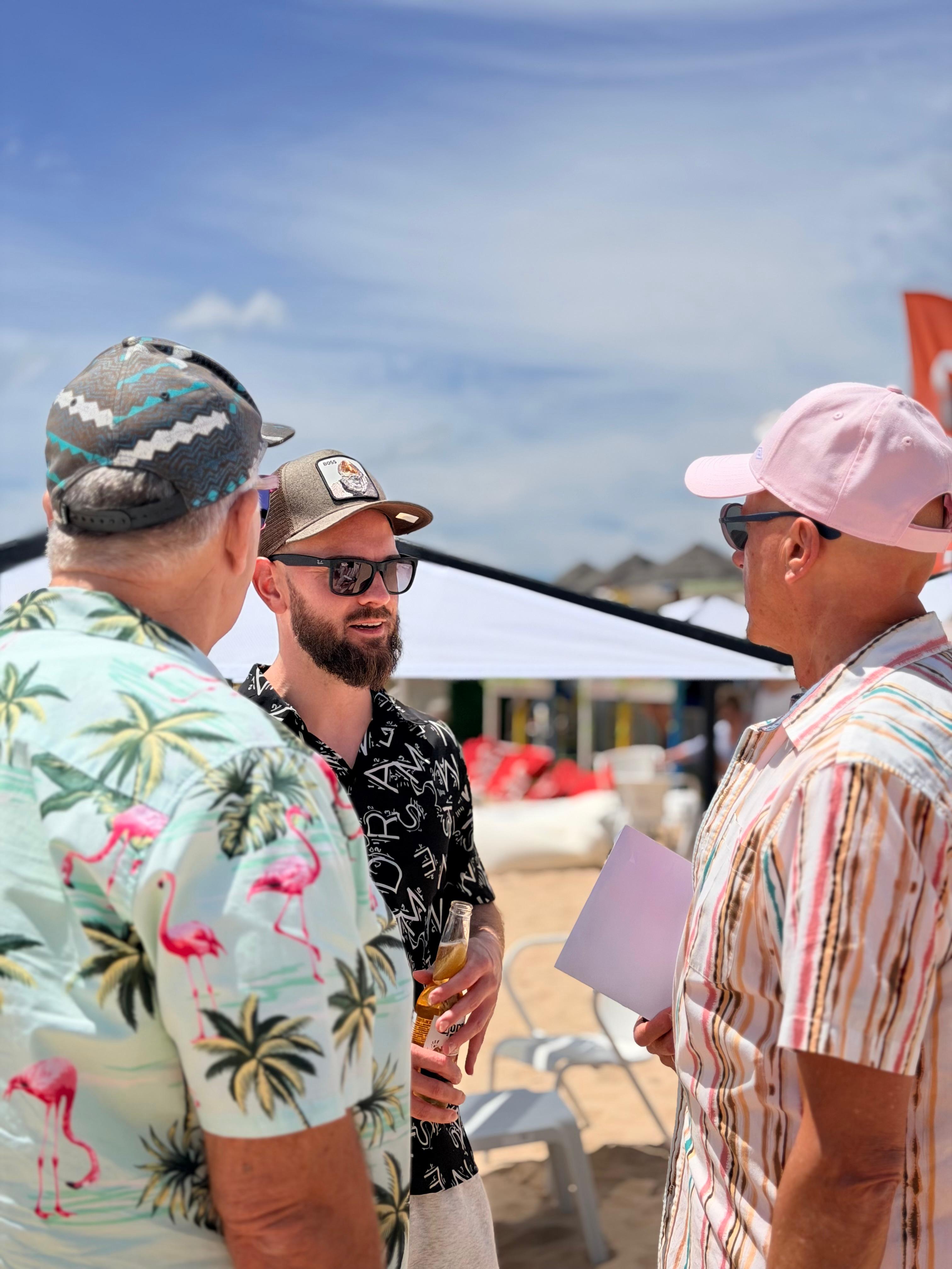 Três convidados com camisas floridas a conversar no Pirata Beach Bash, na Meia Praia.